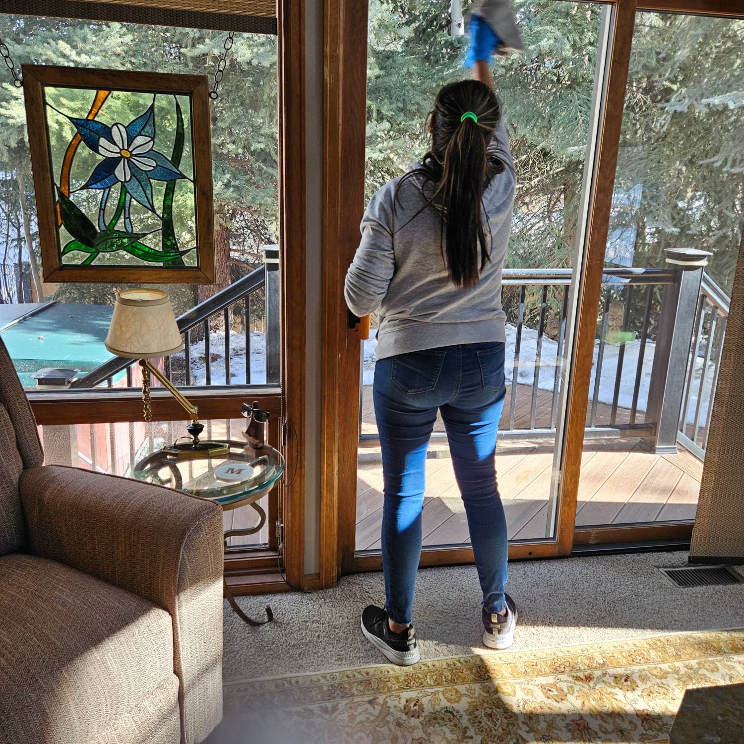 Marina cleaning a sunlit sliding glass door in a Denver living room, snow on the deck outside